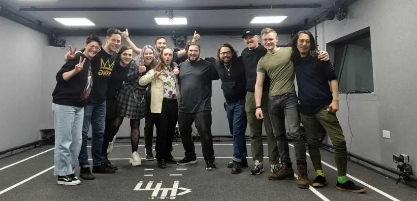 Keith Higinbotham in the centre of a posed group photo, with adults either side of him, all stood in a line, smiling at the camera.