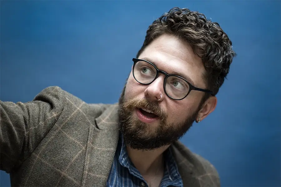 Keith Higinbotham wearing a brown tweed style jacket. He is looking away from the camera holding his right arm up, as if pointing at something but the photo is cropped tight.