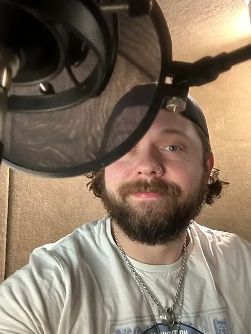 Keith Higinbotham behind a studio microphone. Part of his face is obscured by the mic pop shield.